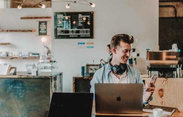 Man in cafe using phone and laptop